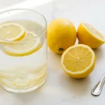 Glass of fresh lemon water with lemon slices on a white marble surface