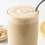 Close-up of oatzempic drink in a glass with a metal straw, rolled oats and lemon in background