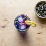 Glass of color-changing Brazilian Mounjaro tonic made with butterfly pea flower, lemon, and ice, garnished with a lemon wheel