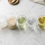 Seven viral weight-loss drinks in small glass tumblers arranged on a white marble surface